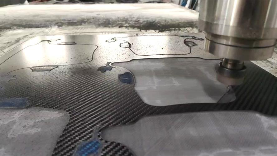 A robotic arm with a coated blade cutting a sheet of carbon fiber