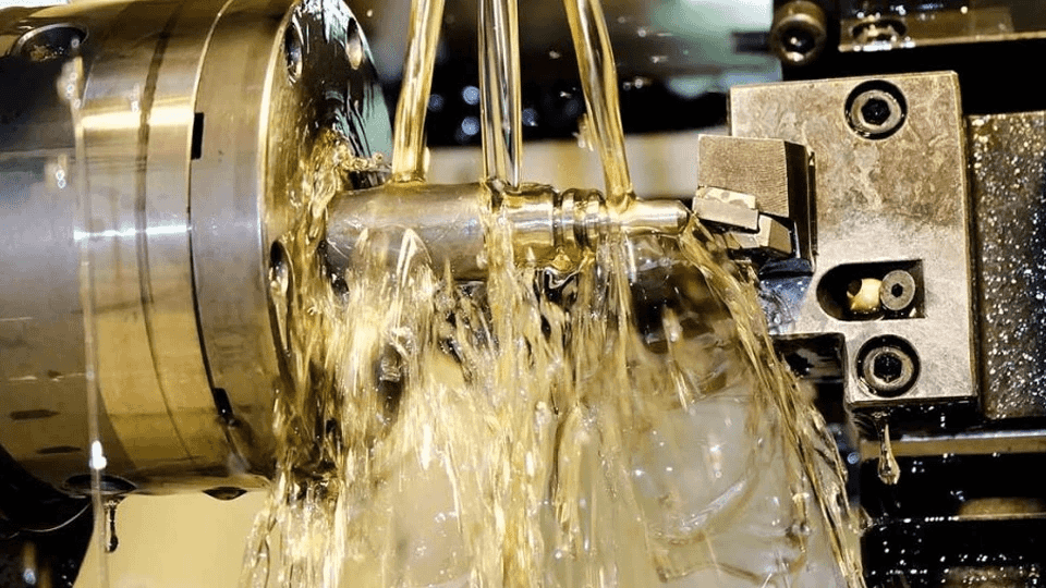 A close-up of an industrial blade cutting through metal with liquid coolant splashing.