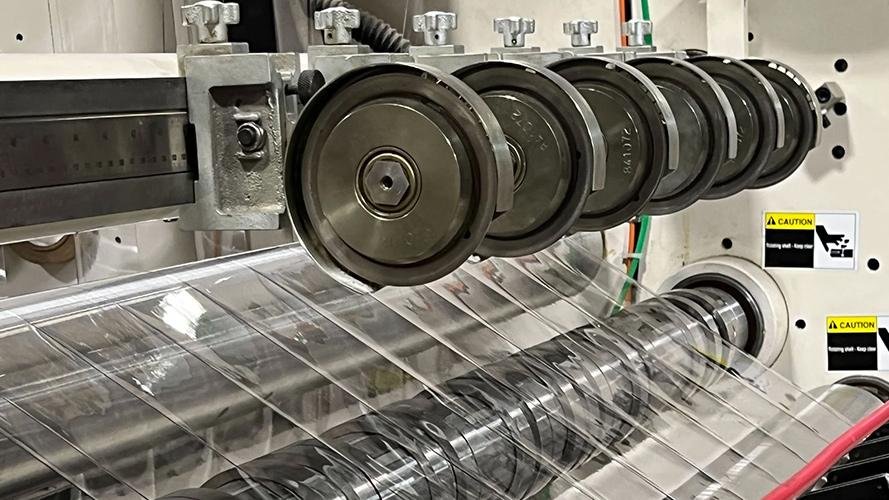 A blade slitting a large roll of plastic film at high speed