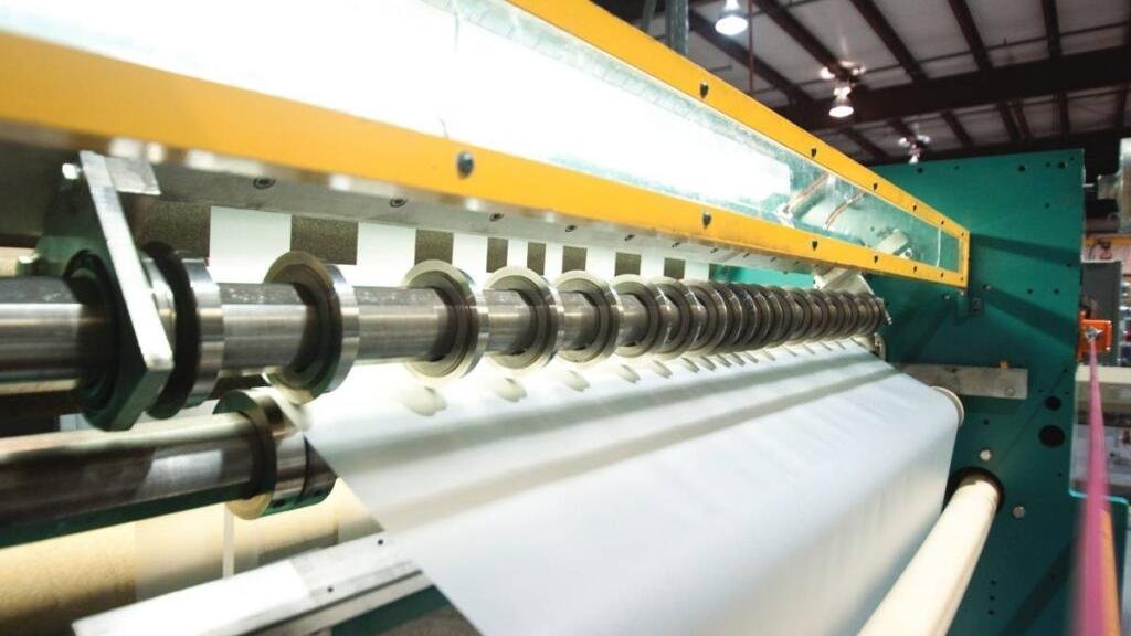A roll of thin plastic film being cut perfectly by an industrial machine.